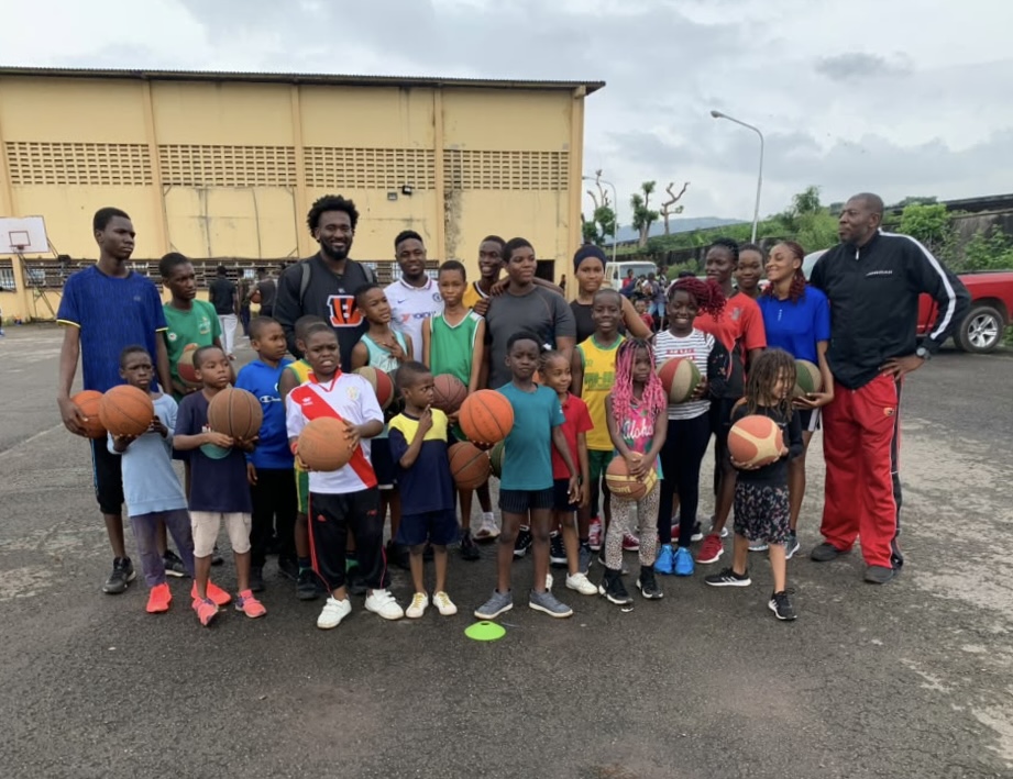 Eric Okenchi with a group of young campers and coaches holding basketballs on an outdoor court