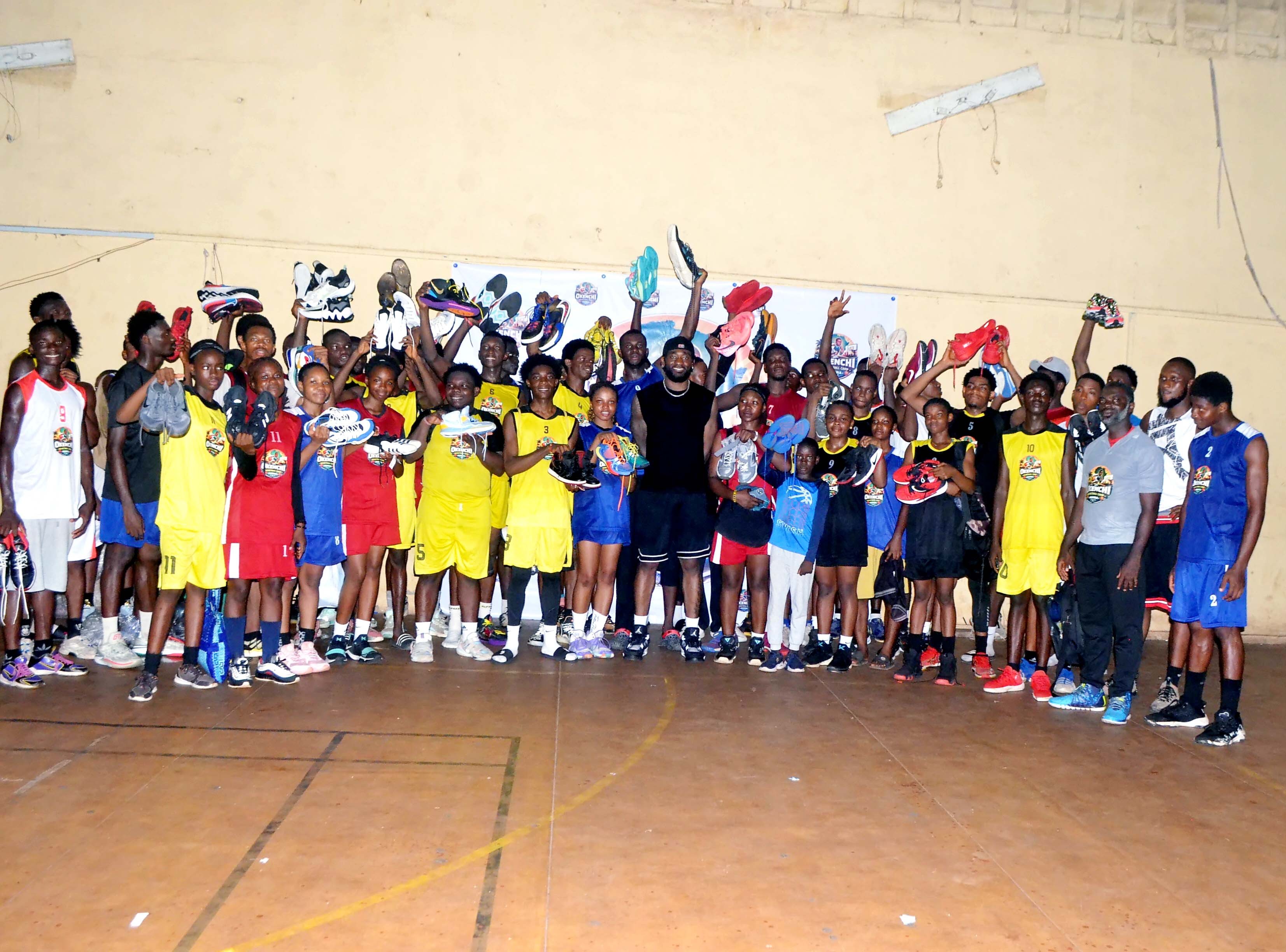 Eric Okenchi with young athletes holding up donated basketball shoes
