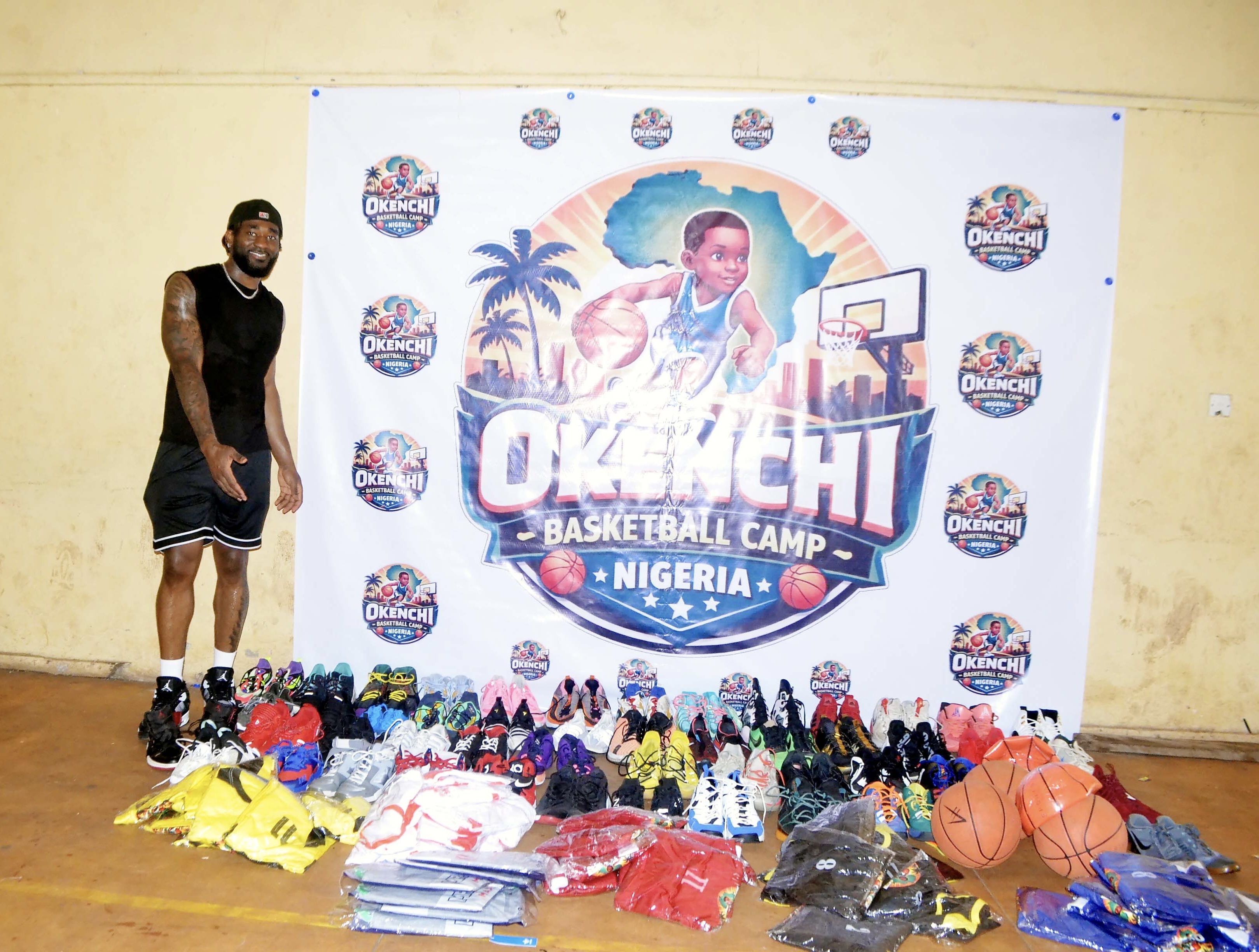 Eric Okenchi beside donated shoes and equipment in front of the camp banner