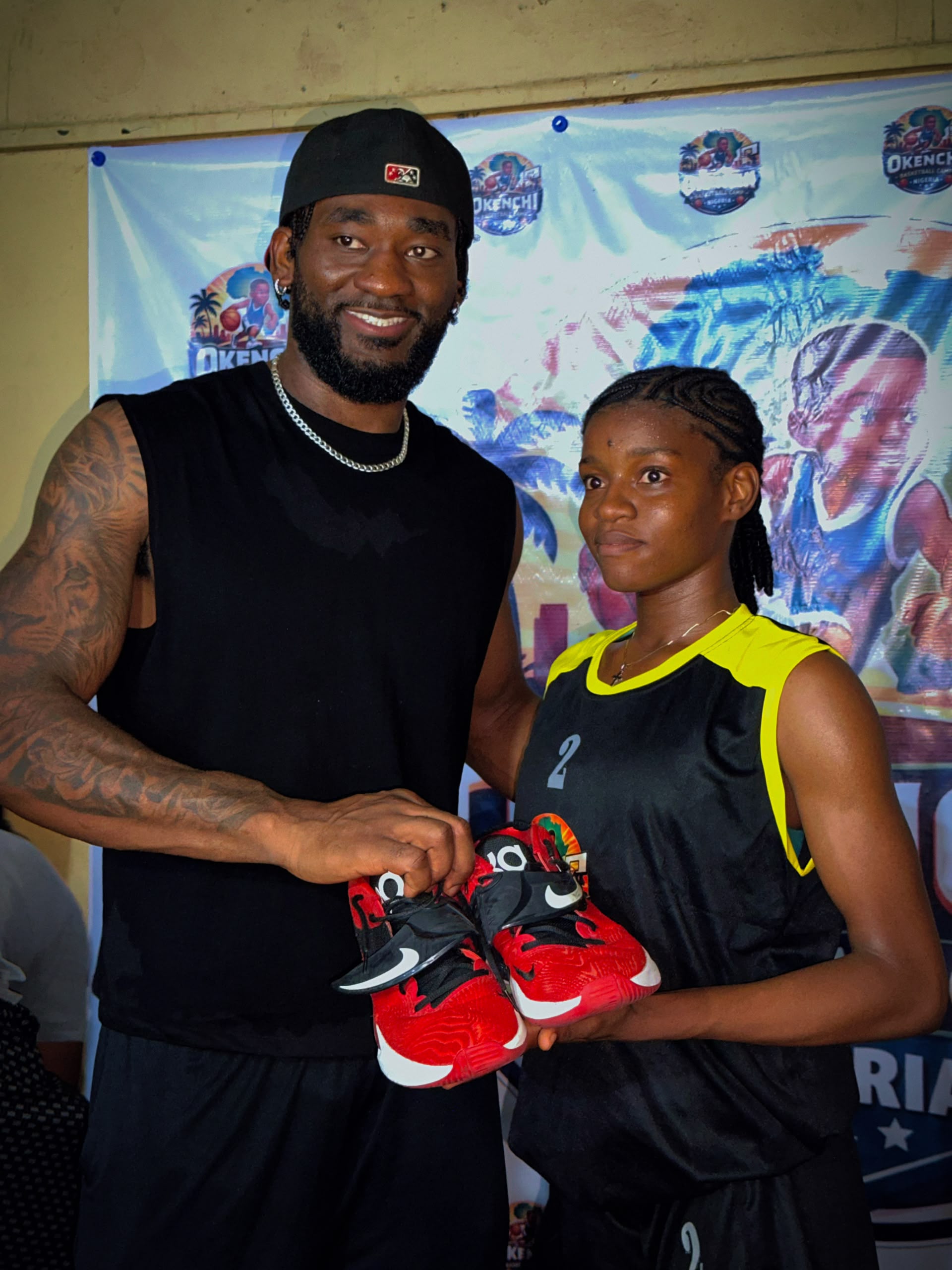Eric Okenchi presenting red and black basketball shoes to a camper