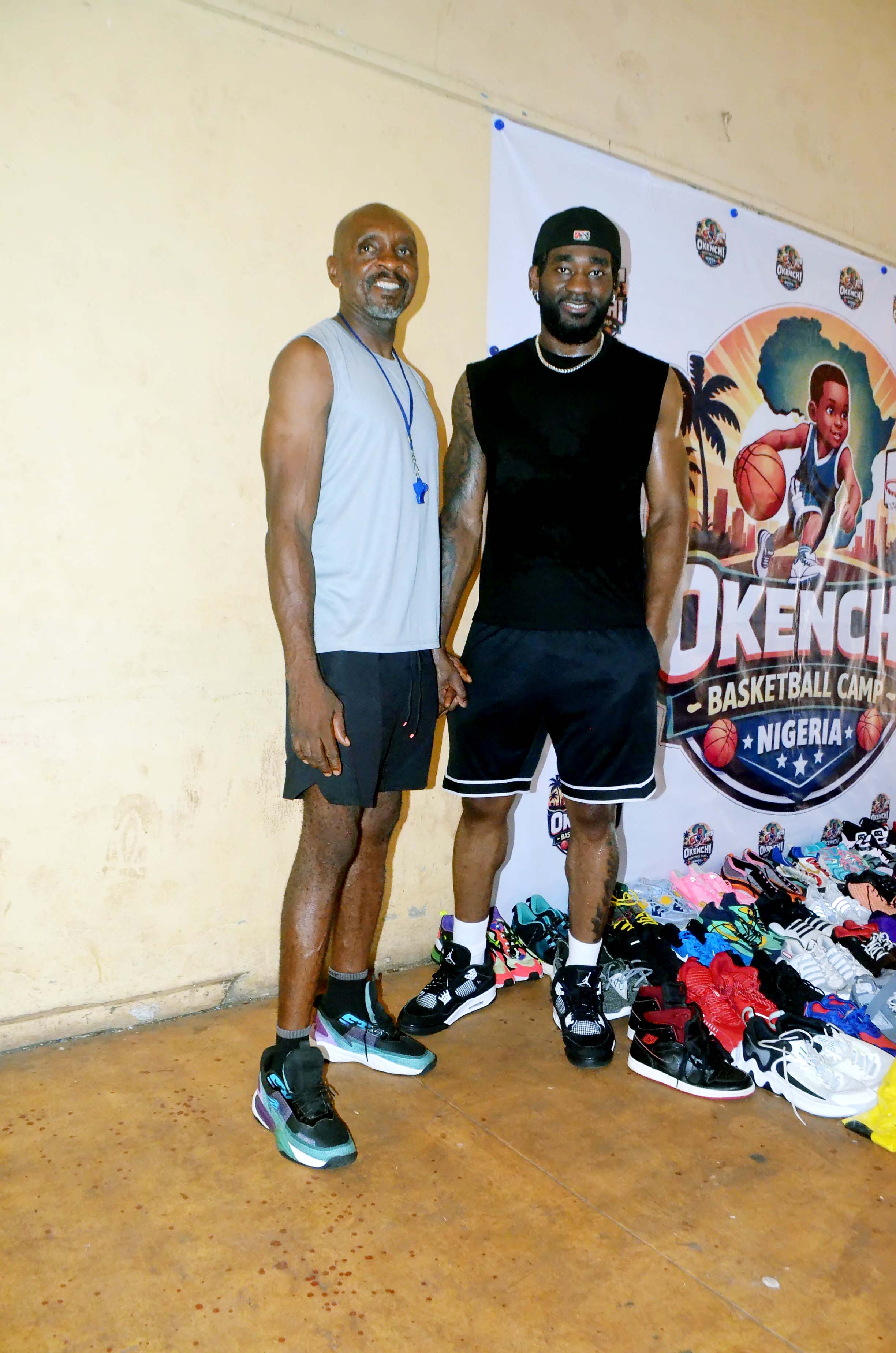 Eric Okenchi with a coach next to rows of donated basketball shoes