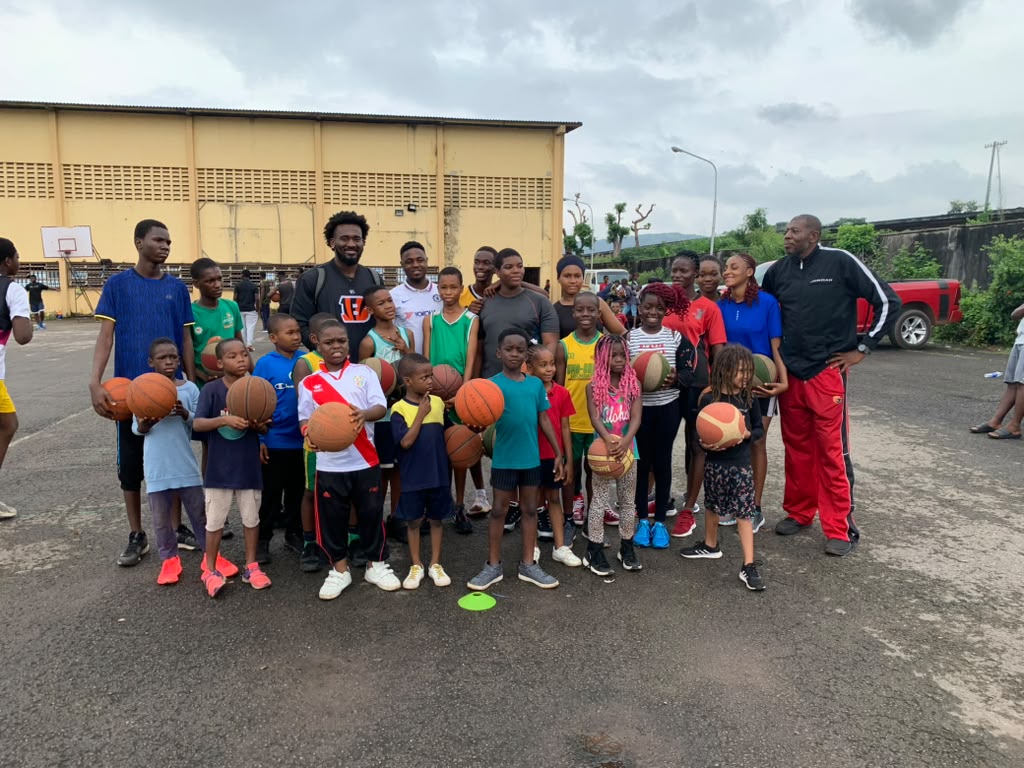 Eric Okenchi with young campers and coaches holding basketballs on an outdoor court