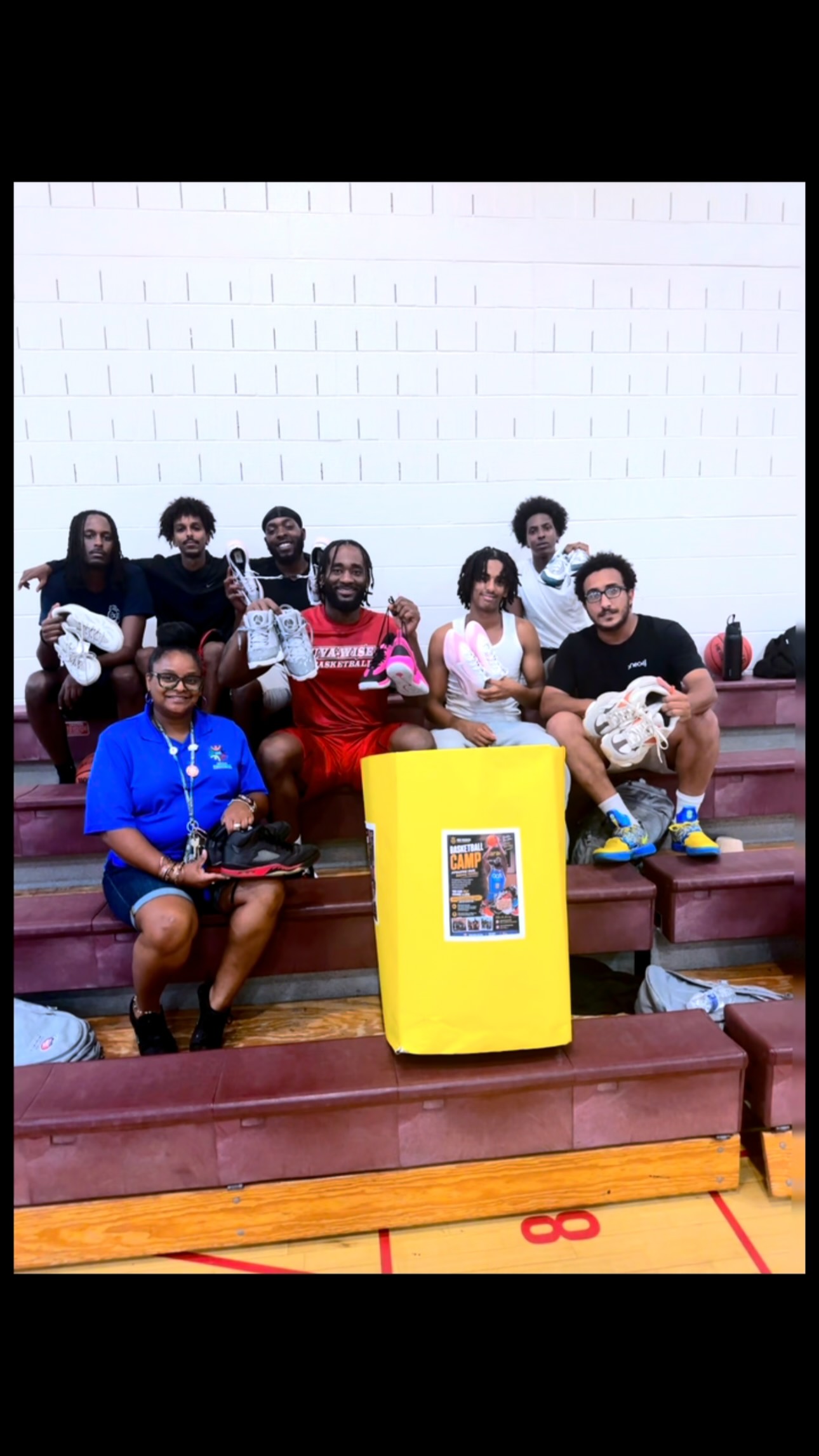 Eric Okenchi with players and staff in a gym, holding up donated shoes